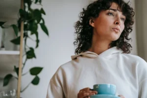 Mujer reflexionando con una taza mientras explora sentimientos de no ser suficiente y dudas sobre sí misma.