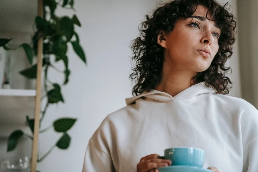 Woman reflecting with a cup while exploring feelings of not being enough and self-doubt.